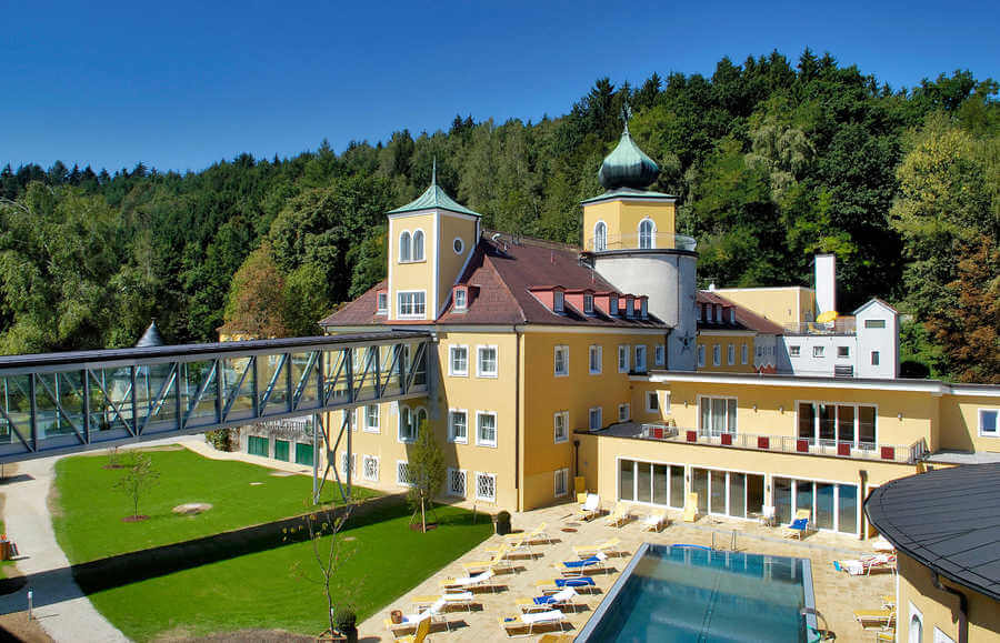 Gebäude mit Pool und Liegen, dahinter Wald